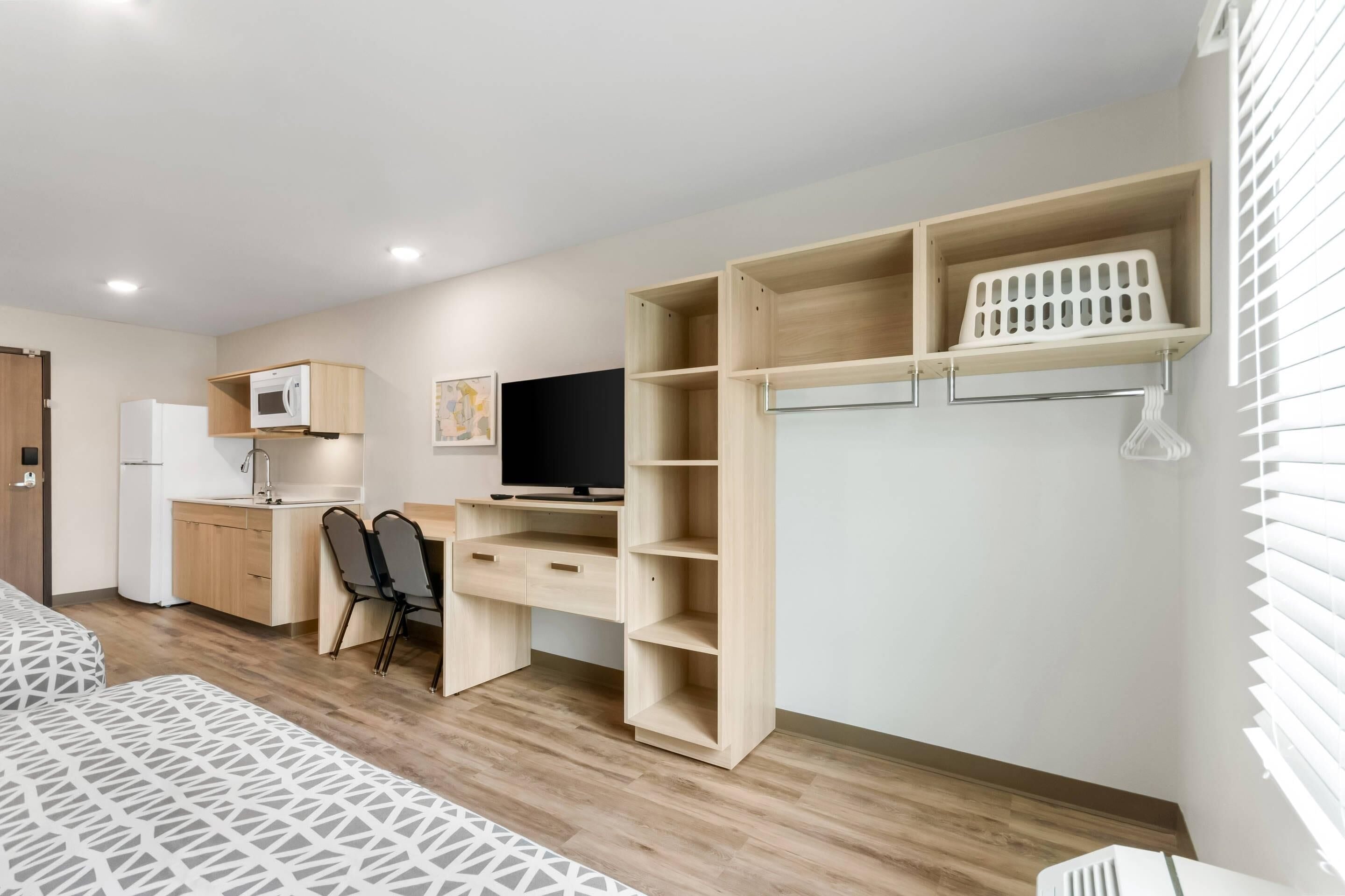 A modern, well-lit room with a kitchenette, a desk with a computer, and a TV.