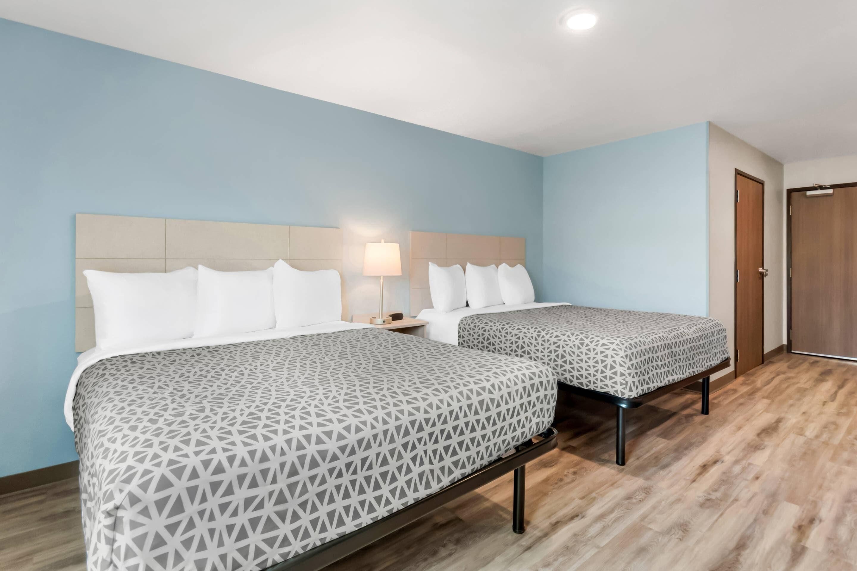 A hotel room with two beds, a nightstand, a lamp, and a wooden door.