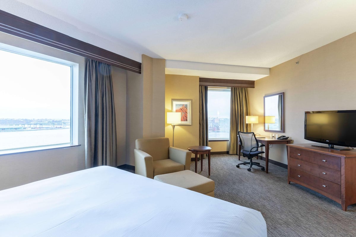A hotel room with a large bed, a desk with a television, a chair, and a small table.