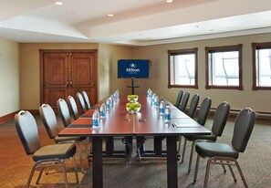 A conference room with a long table, chairs, a TV screen, and a window.