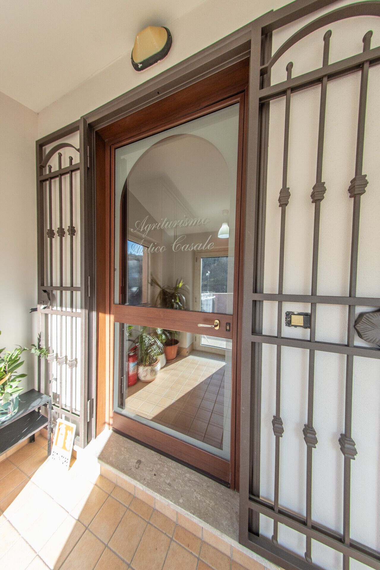 Una porta in legno con un pannello di vetro e inferriate, che dà su un patio piastrellato con piante in vaso.
