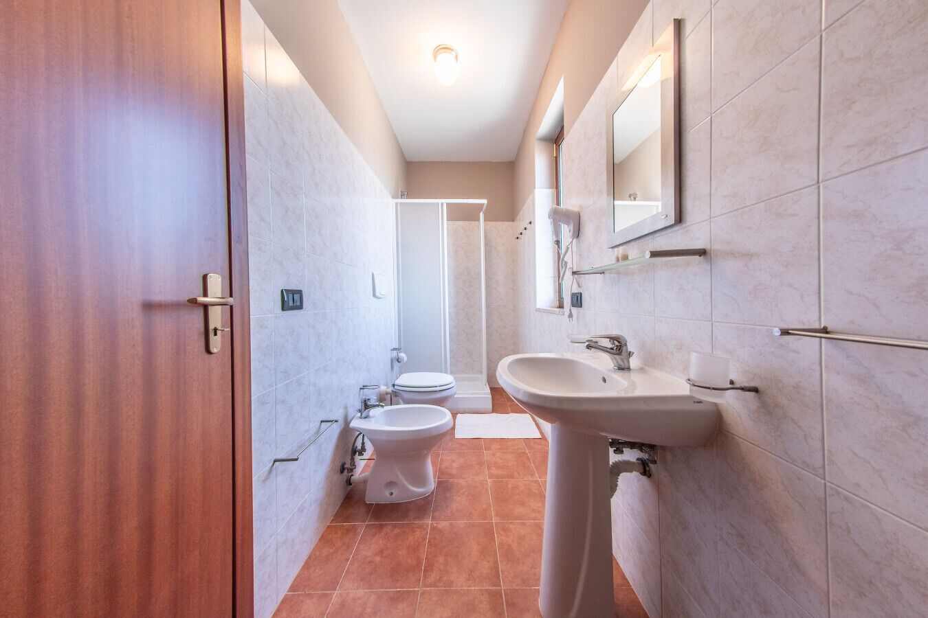Une salle de bain avec une porte en bois, un lavabo sur colonne, des toilettes et un espace douche.