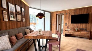 Un salon moderne avec un mur en bois, un canapé, une table à manger, des chaises, un téléviseur et une grande fenêtre.