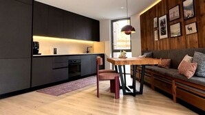 Une cuisine moderne avec des meubles de couleur sombre, une table à manger en bois et un canapé avec des coussins.