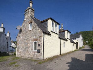 Une rangée de maisons en pierre et en briques, avec des cheminées, une route pavée et un ciel bleu dégagé.