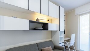 A modern living room with a grey sofa, a white chair, and built-in white shelving. - Cosy apartment for 2 people with A/C, WIFI and balcony (Sanremo)