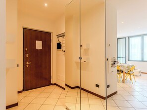 Ein Hotelzimmer mit Holztür, Glastrennwand, Fliesenboden und einem Essbereich mit gelben Stühlen und einem Tisch.