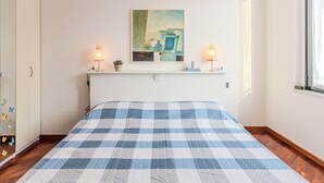 A bedroom with a checkered bedspread, two bedside lamps, a small potted plant, and a painting on the wall. - Cosy apartment for 2 guests with WIFI, patio, pets allowed and panoramic view (Como)