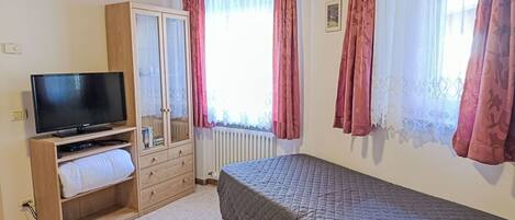 Une chambre à coucher avec un lit, une télévision, une armoire et une fenêtre avec des rideaux.