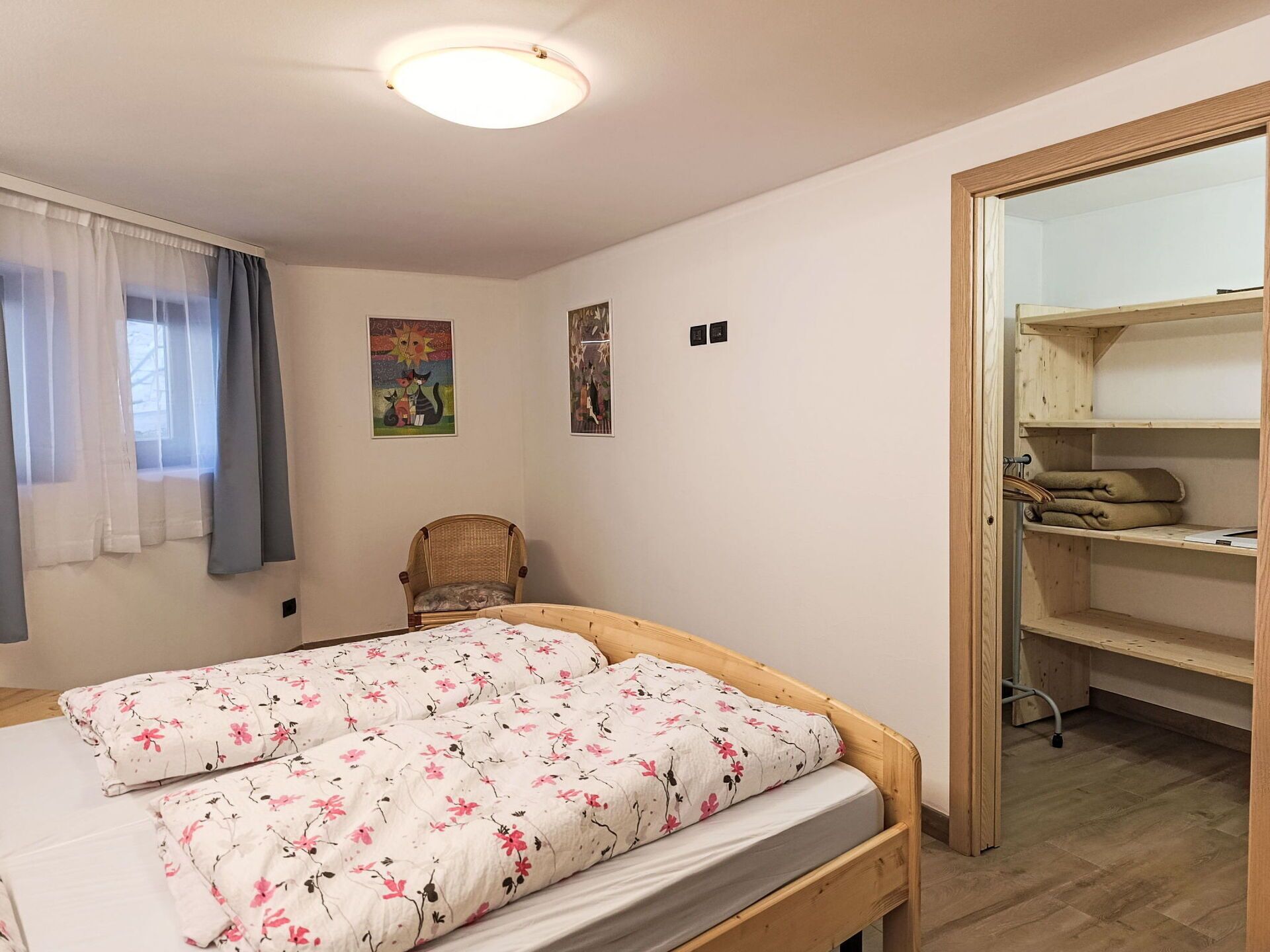 Ein Schlafzimmer mit einem hölzernen Bett, einem Sessel, einem Kleiderschrank und zwei an der Wand befestigten Lichtschaltern.