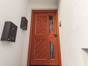 A wooden door with a glass panel, a mailbox, and a wall-mounted light fixture. - Beautiful apartment for 4 guests with TV (Campitello Di Fassa)