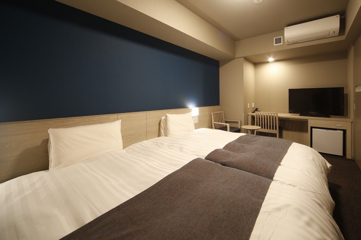 Quarto de hotel com uma cama grande, uma escrivaninha com televisão e um ar condicionado.
