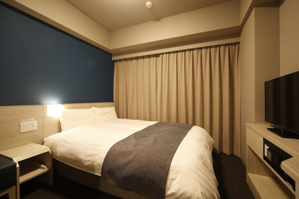 Ein Hotelzimmer mit Bett, Nachttisch, Fernseher und Vorhängen.