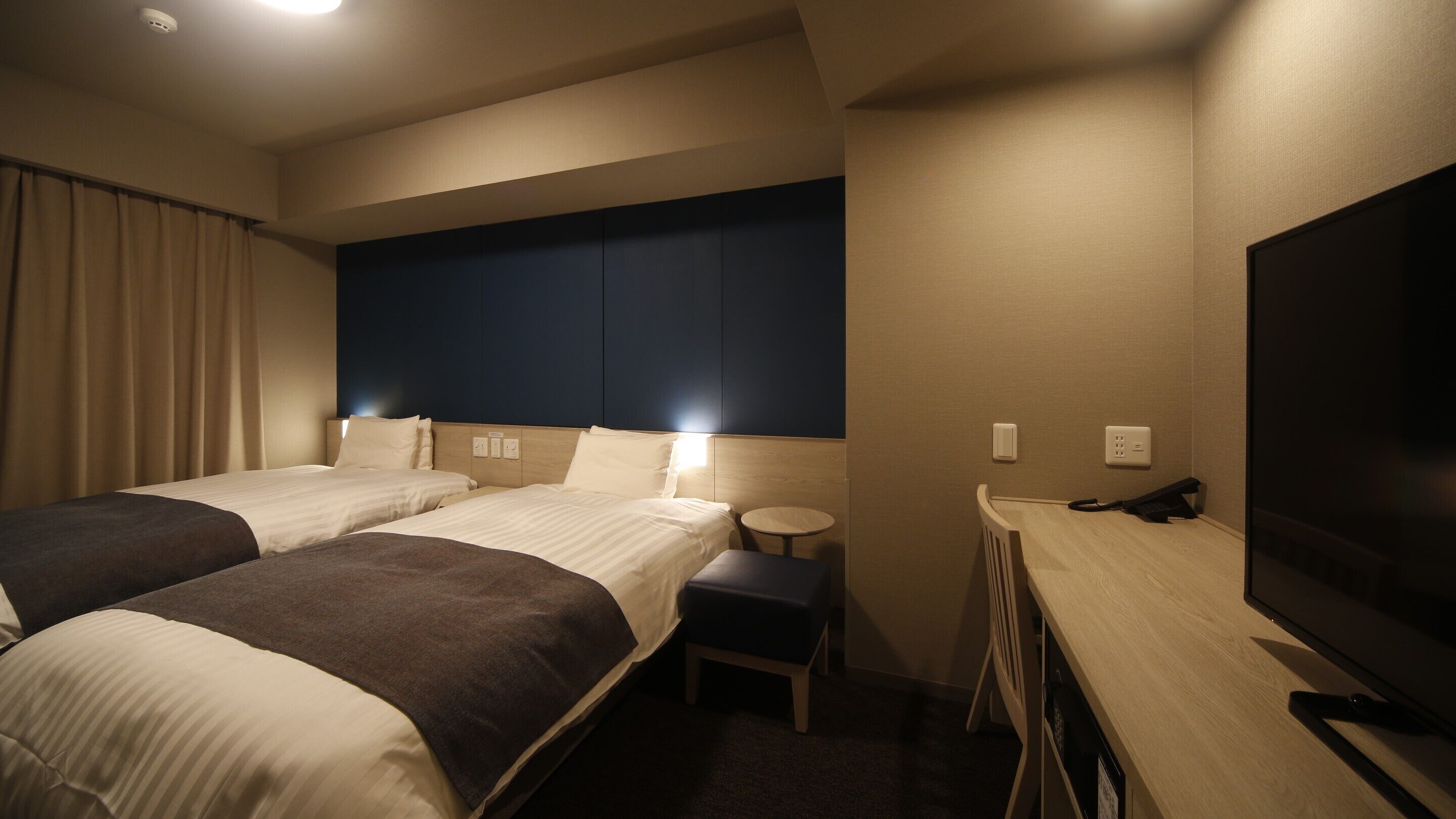 A hotel room with two beds, a desk with a chair, a television, and a small table.