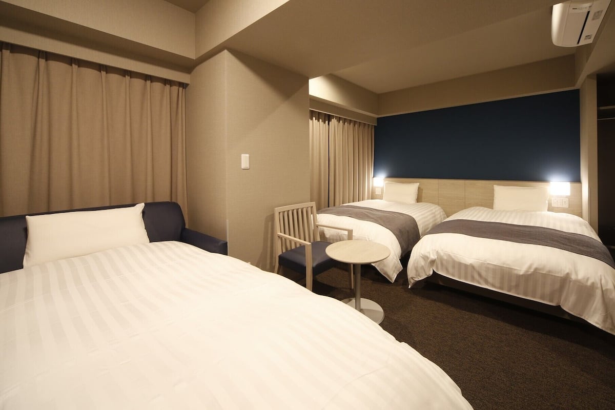 Ein Hotelzimmer mit zwei Betten, einem Sessel, einem kleinen Tisch und einem Kleiderschrank.