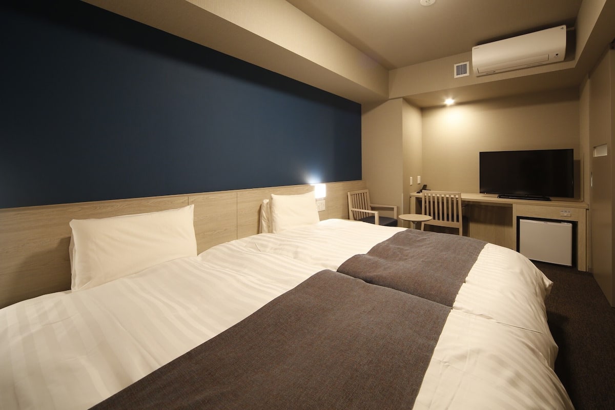 Ein Hotelzimmer mit einem Bett, einem Schreibtisch, einem Sessel, einem Fernseher und einer Klimaanlage.