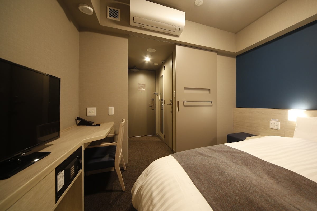 Ein Hotelzimmer mit Bett, Schreibtisch mit Fernseher, Tür und Klimaanlage.