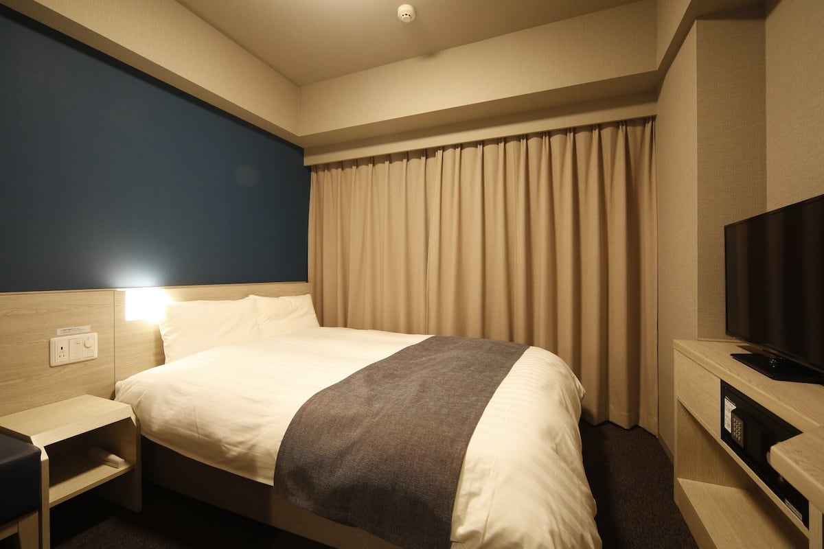 Ein Hotelzimmer mit Bett, Nachttisch, Fernseher und Vorhängen.