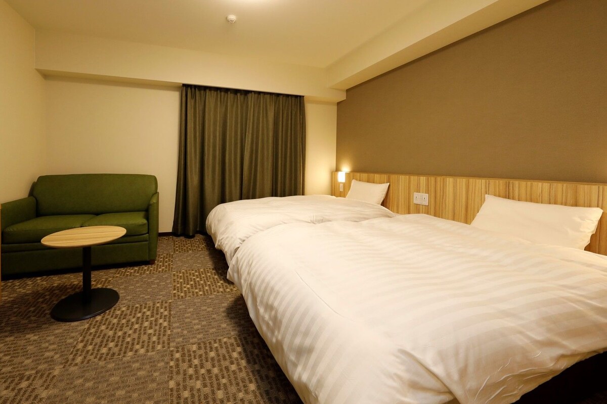 A hotel room with a bed, a television, a green armchair, and a small table.