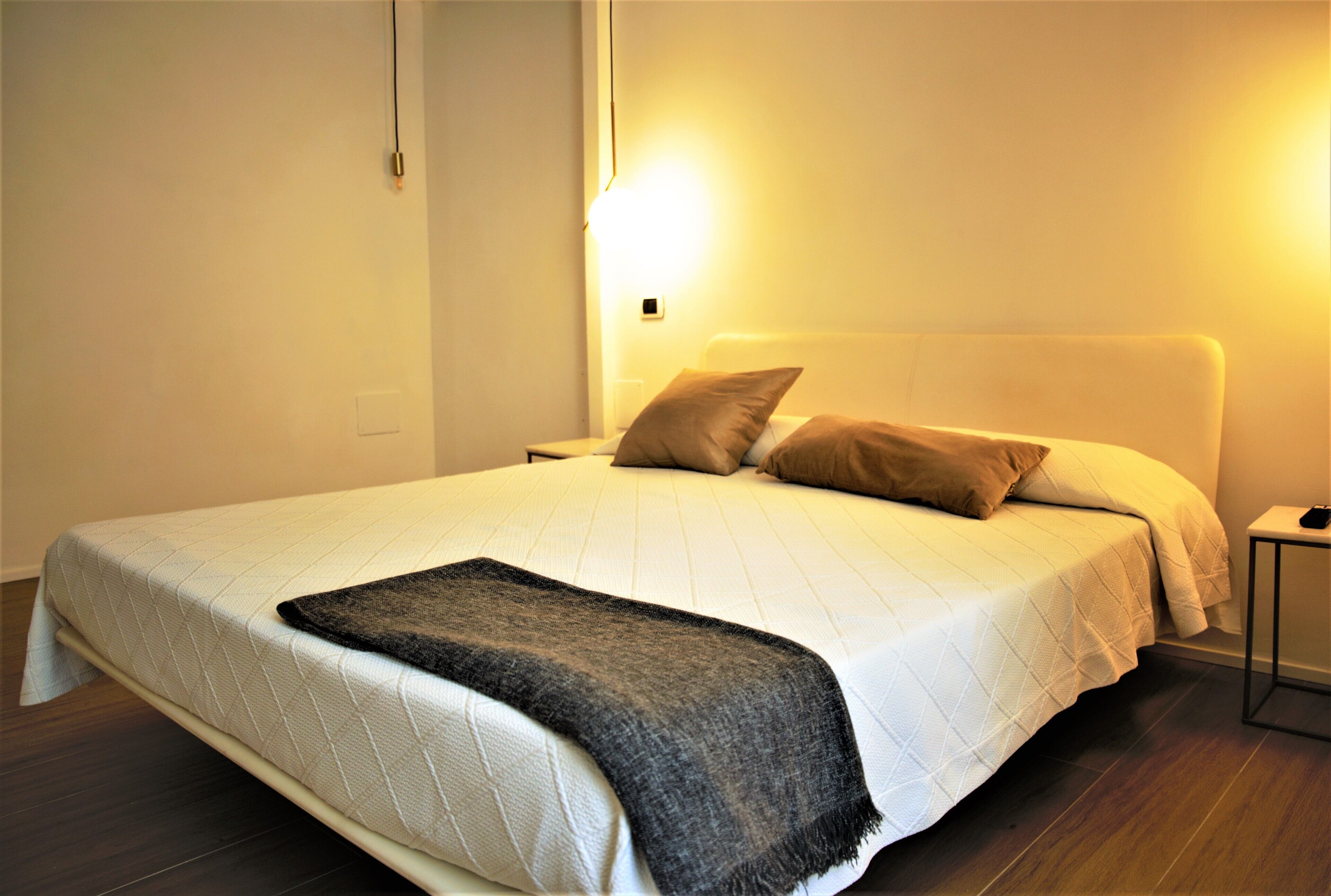A neatly made bed with a white duvet and two pillows, a dark throw blanket, and a bedside table with a lamp.