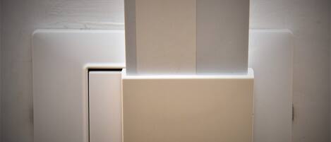 Pared blanca con un interruptor de luz y un objeto rectangular, quizás una tarjeta o una etiqueta, insertado en una ranura.