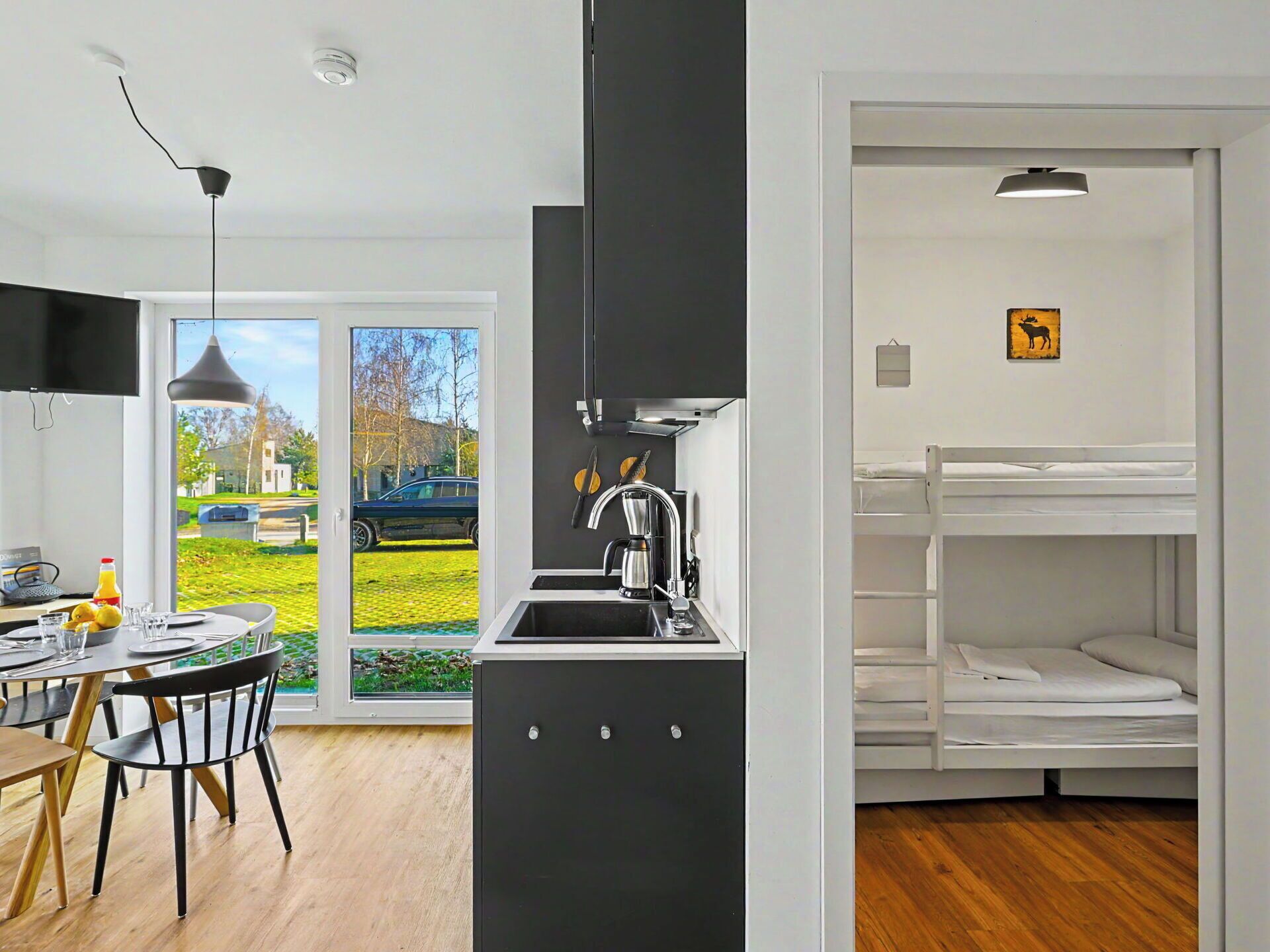 A modern kitchen with a sink, a dining area with a table and chairs, and a bunk bed with a white mattress.