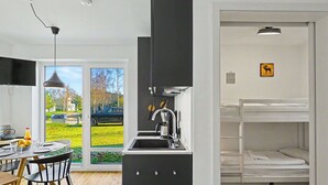 Eine moderne Küche mit Spüle, ein Essbereich mit Tisch und Stühlen sowie ein Etagenbett mit weißer Matratze.