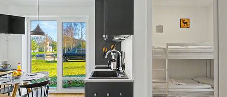A modern kitchen with a sink, a dining area with a table and chairs, and a bunk bed with a white mattress.