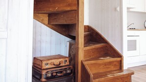 A wooden staircase leading to a loft area with white paneled walls and a kitchen visible in the background. - House with 2 bedrooms near of the forest and sea. (Województwo pomorskie)