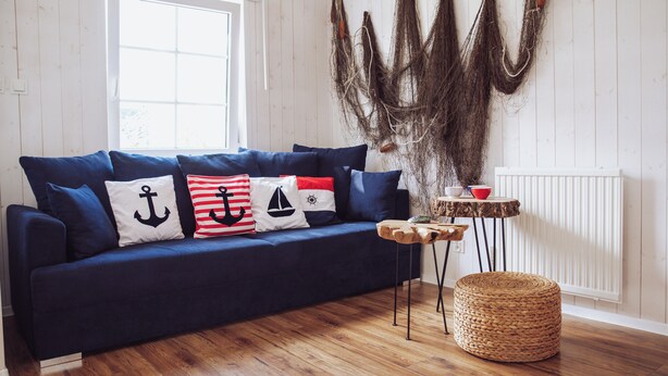 A dark blue sofa with nautical-themed pillows, a woven basket, and a rustic wall hanging. - House with 2 bedrooms near of the forest and sea. (Województwo pomorskie)
