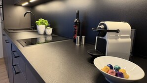 A modern kitchen with a black countertop, a built-in sink, a wine bottle, a coffee machine, and a bowl of colorful items. - Cosy apartment for 4 guests with WIFI, TV and balcony (Zell Am See)