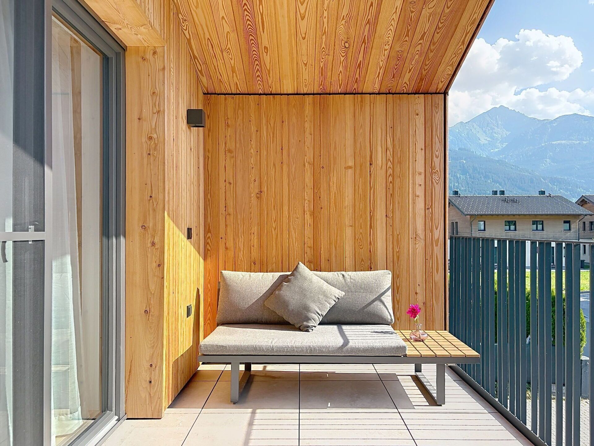 A wooden balcony with a built-in bench and cushions, overlooking a mountainous landscape.
