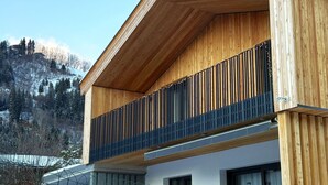 A modern building with wooden exterior panels, a balcony with metal railings, and a view of snow-covered mountains. - Cosy apartment for 4 guests with WIFI, TV and balcony (Zell Am See)
