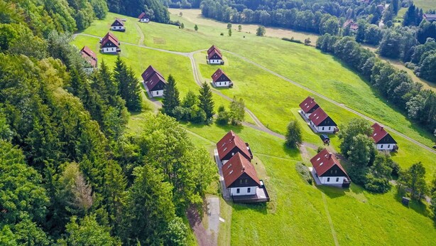 Oversigtsbillede af en landlig landsby med traditionelle huse tæt sammen på grønne marker, omgivet af skovklædte bakker.