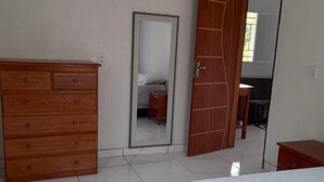 Ein Schlafzimmer mit einem Bett, einer Holzkommode, einem Spiegel und einem Kleiderschrank.