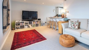 Ein modernes Wohnzimmer mit einem großen Flachbildfernseher, einem roten Teppich mit Muster, einem weißen Sofa und einem hölzernen Ottomanen.