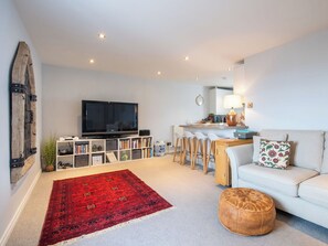 Ein modernes Wohnzimmer mit einem großen Flachbildfernseher, einem roten Teppich mit Muster, einem weißen Sofa und einem hölzernen Ottomanen.