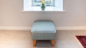 Ein Zimmer mit Fenster, einer kleinen Bank und einer Vase mit Blumen.