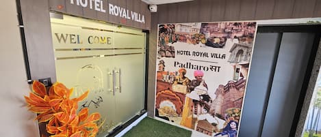 La entrada del Hotel Royal Villa, con un letrero que dice 'Welcome', un cartel de Padharosa y una cámara de seguridad sobre la puerta.