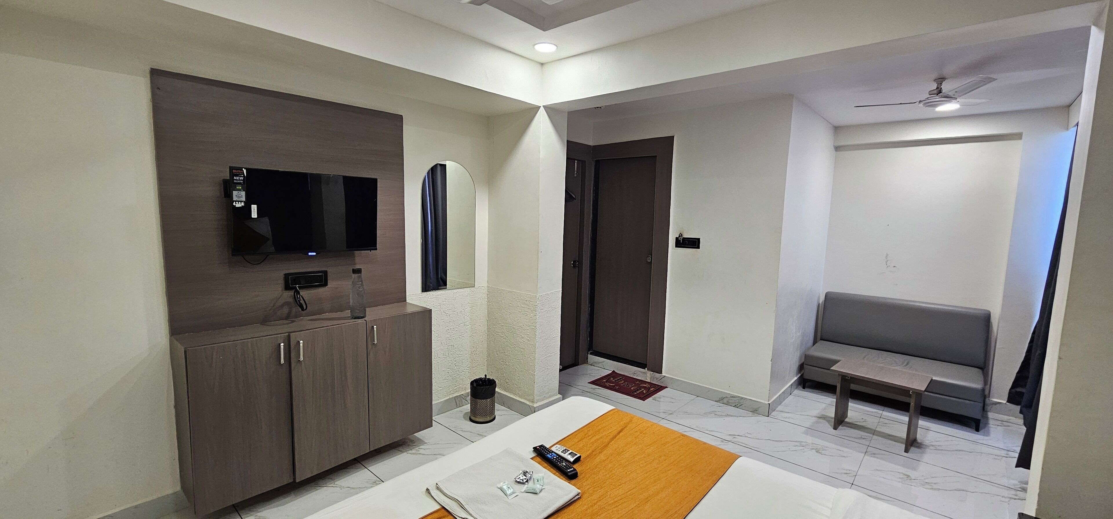 A modern hotel room with a flat-screen TV, a sofa, a small table, and a ceiling fan.