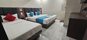 Habitación de hotel con dos camas, cada una con cabecero, ropa de cama blanca y almohadas azules y rojas.