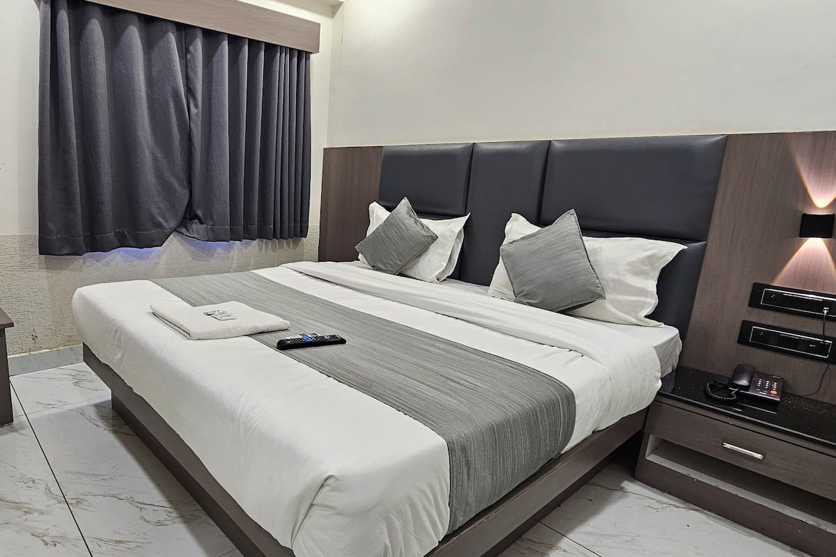 A modern hotel room with a large bed, bedside tables, a nightstand, a remote control, and a phone on the nightstand.