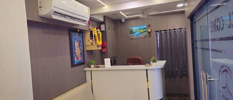 A reception area with a white counter, a ceiling fan, a clock, and a painting on the wall.
