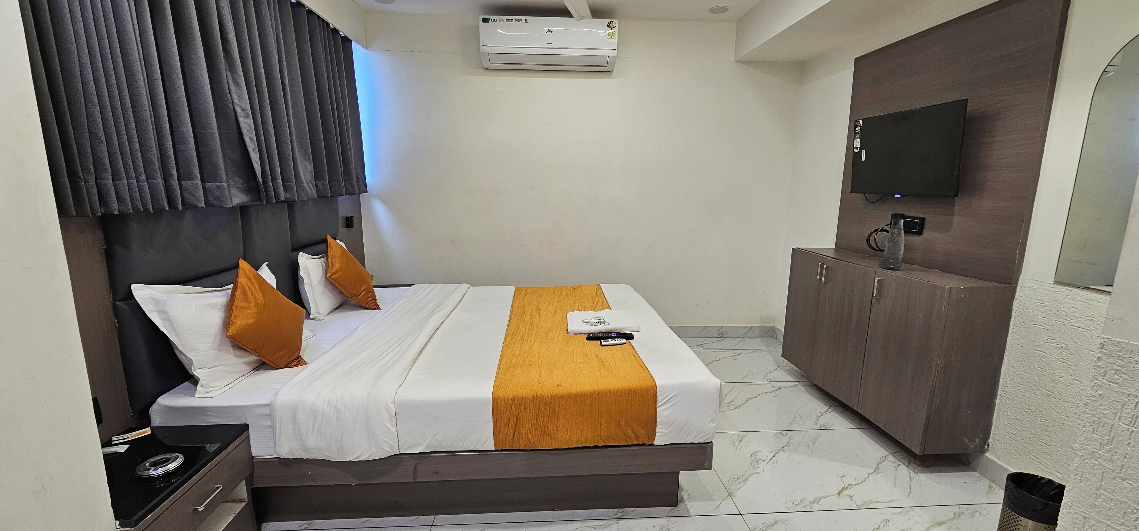 A hotel room with a bed, a television, an air conditioning unit, and a cabinet.