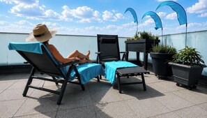 Een dakterras met twee lounge fauteuils, een bijzettafeltje en potten met planten.