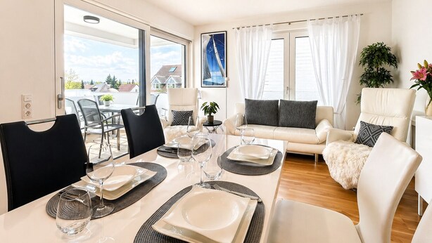 Ein modernes Wohnzimmer mit Essbereich, weißen Möbeln und einem großen Fenster mit Blick.