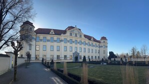 Ein großes, historisches Gebäude mit symmetrischer Architektur, einem zentralen Eingang und einem gepflegten Rasen.