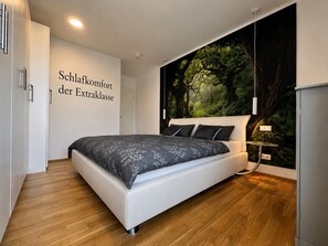 Une chambre moderne avec un grand lit, une fresque murale et une armoire.