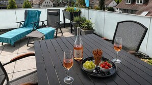 Eine Dachterrasse mit einem Tisch für zwei Personen, einer Weinflasche und einer Platte mit Trauben und Brezeln.