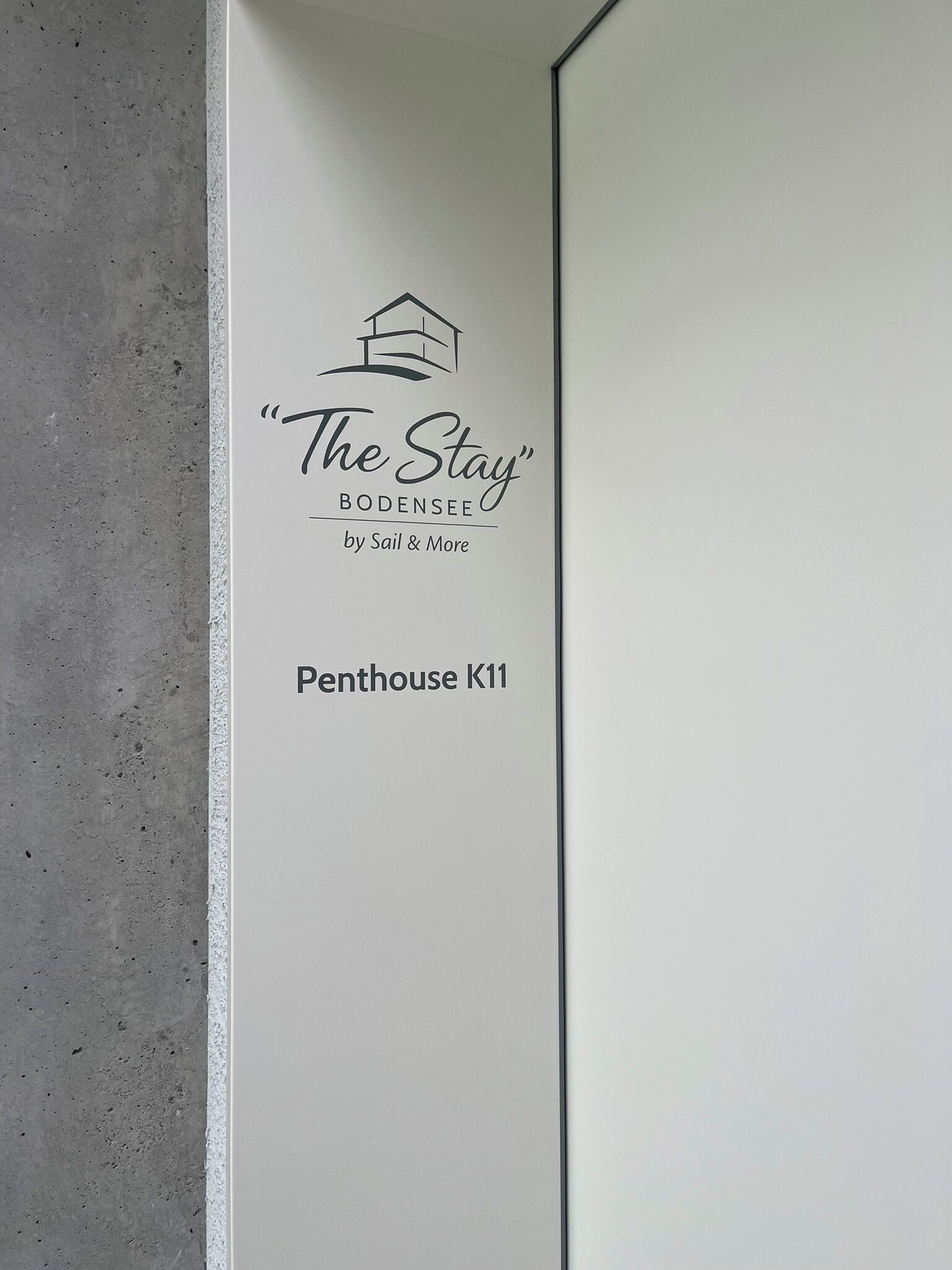 Un mur orné d’un logo et d’une inscription pour « The Stay », une offre de Sail & More, indiquant qu’il s’agit d’un hôtel ou d’un service d’hébergement.